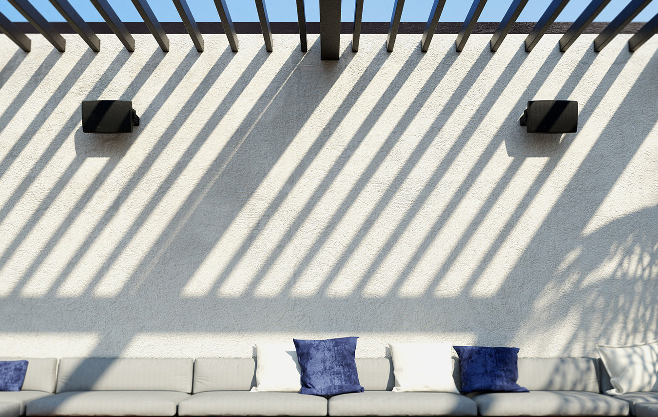 Outdoor patio with a pergola, wall-mounted aperion audio CTOD outdoor/indoor speakers, and a sofa with blue cushions.