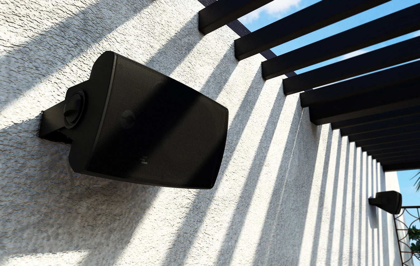 Black outdoor speaker mounted on a wall with a blue sky background