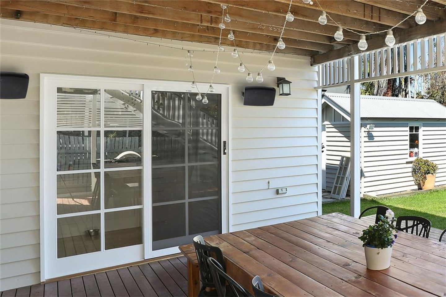 Outdoor patio area with Aperion Audio's Clearus CTOD Outdoor/Indoor speaker. With sliding glass door, wooden deck, and potted plants.
